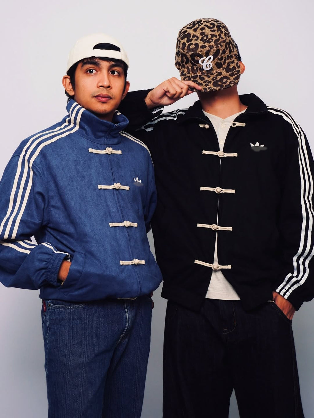 Two people wearing Adidas jackets and hats against a plain background