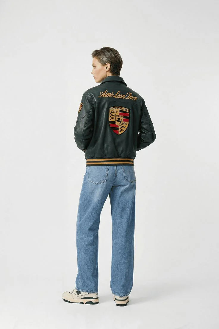 Person wearing a green porsche 933 jacket with a logo on the back, standing against a white background