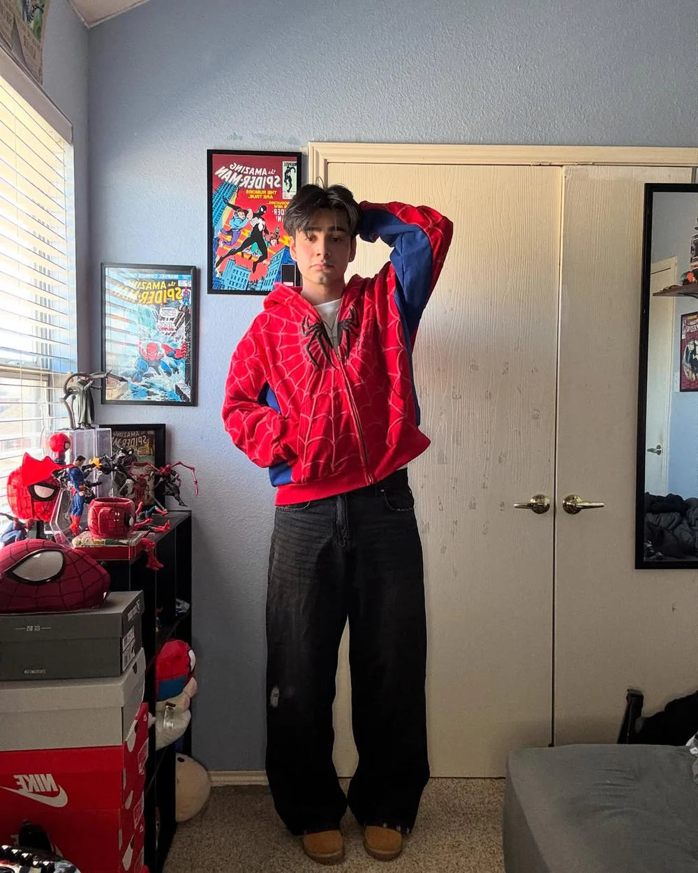 Person wearing a red hoodie with blue sleeves in a room with posters and a bed in the background
