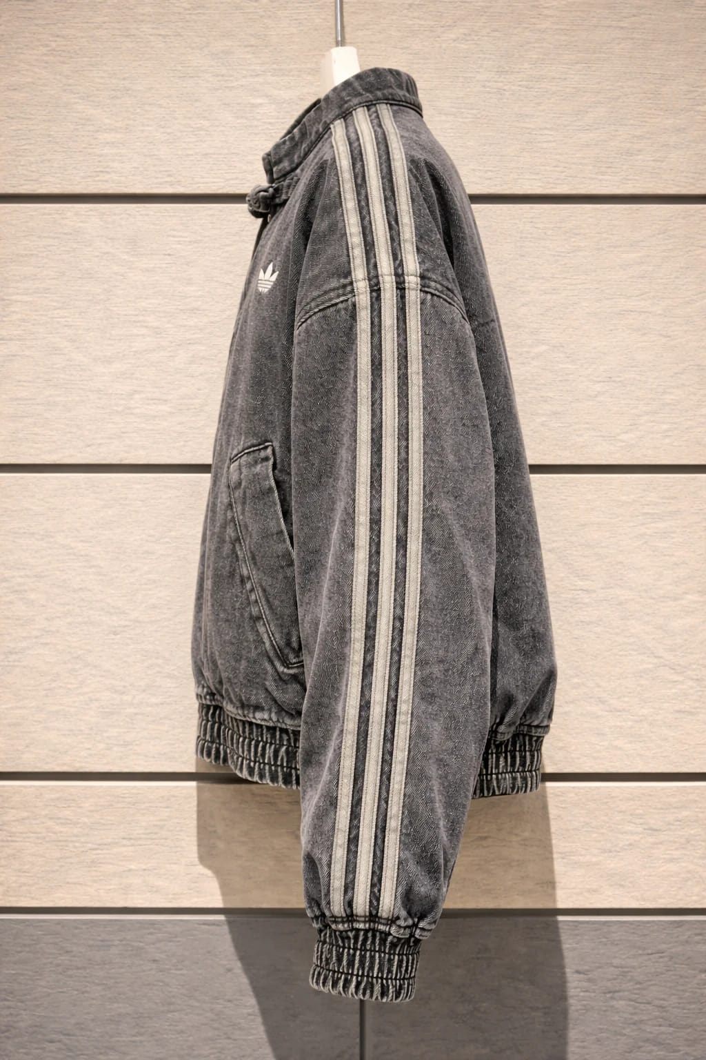 Gray Adidas tracksuit jacket with white stripes on a wooden panel background