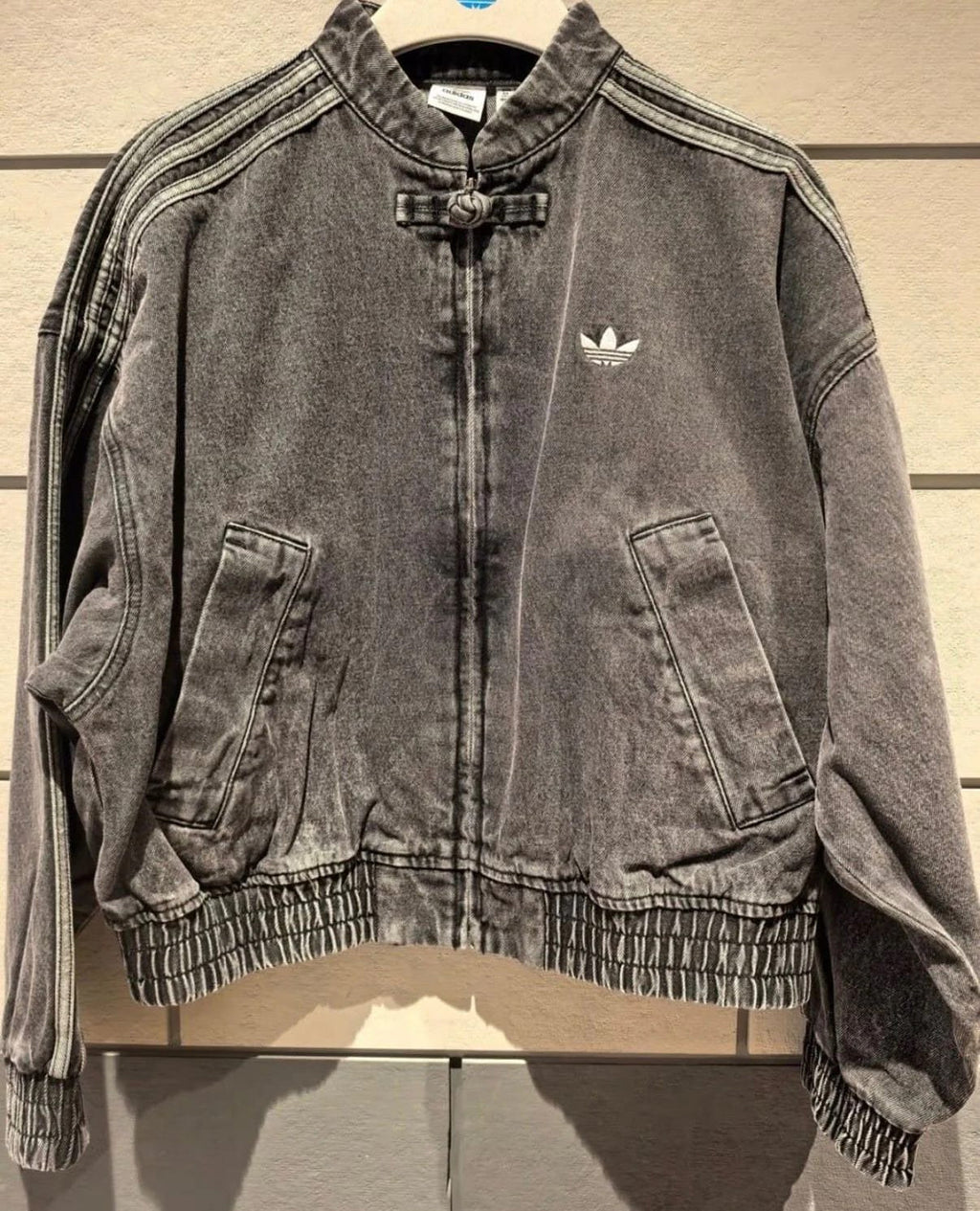 Gray denim jacket with Adidas logo on a wooden surface
